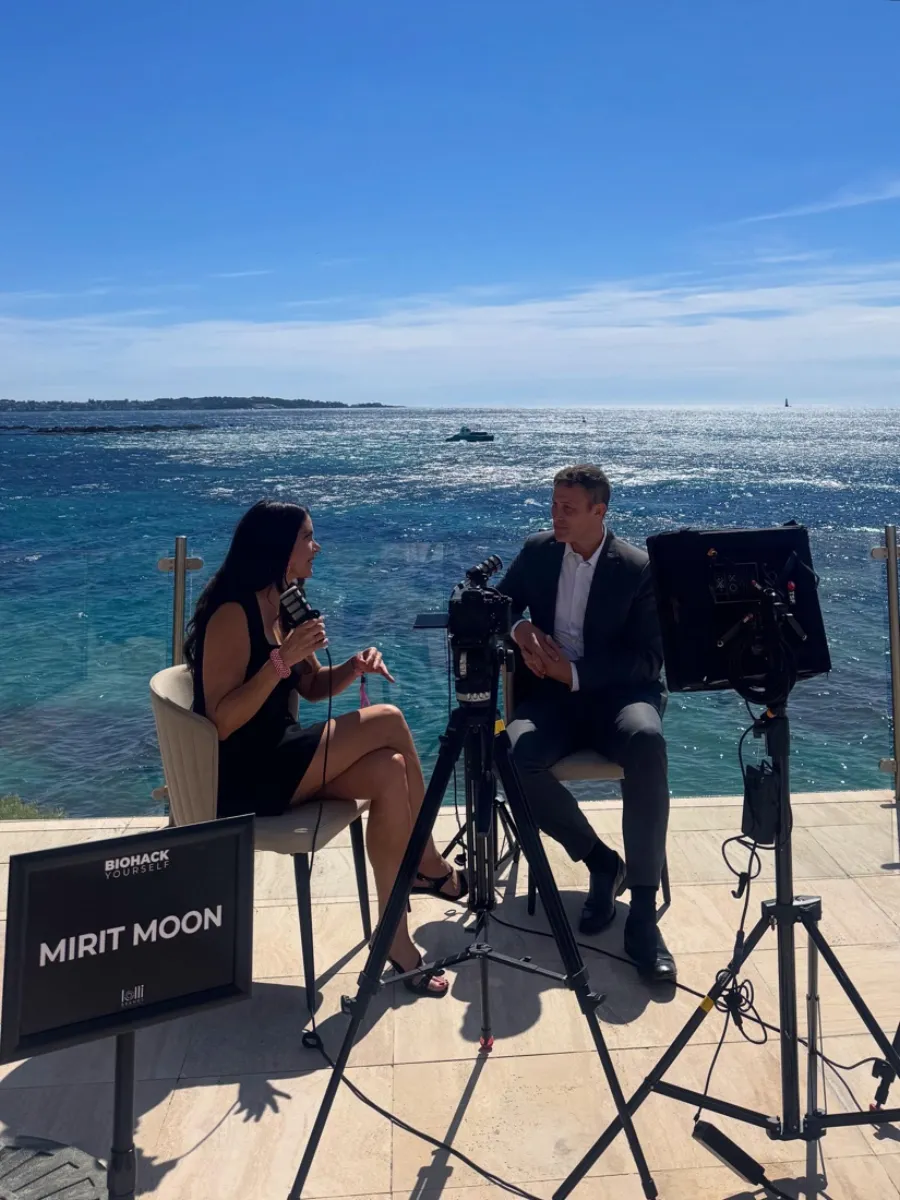 Mirit Moon interviewing a guest on set by the sea